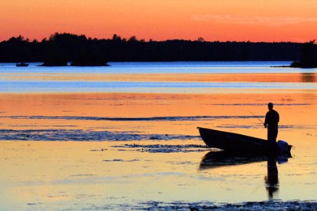 man standing in boat fishing at sunset