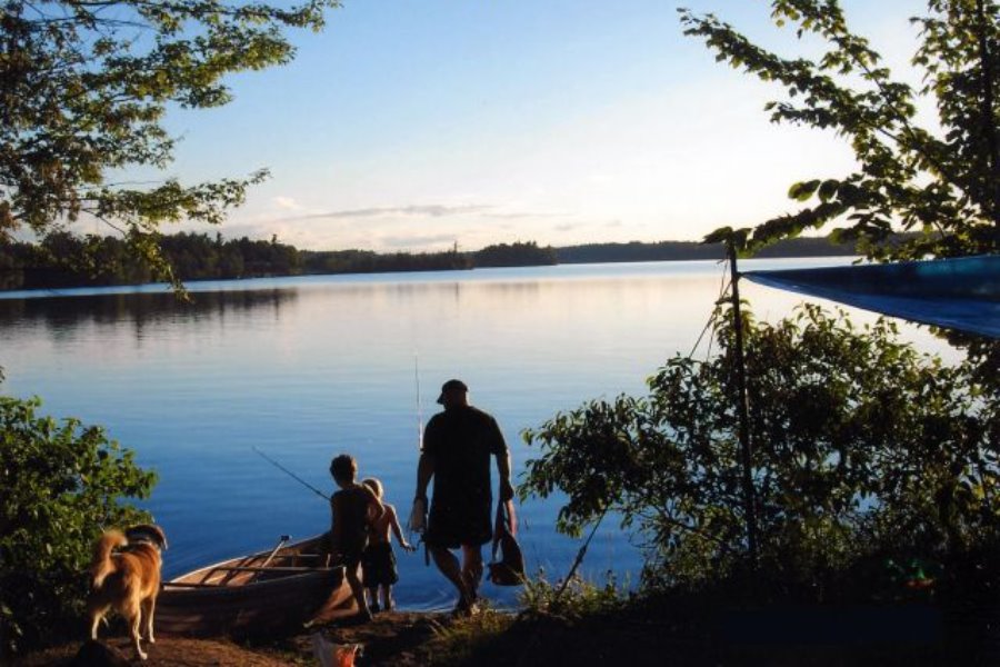 a man, two kids and a dog with fishing rods, launching a boat