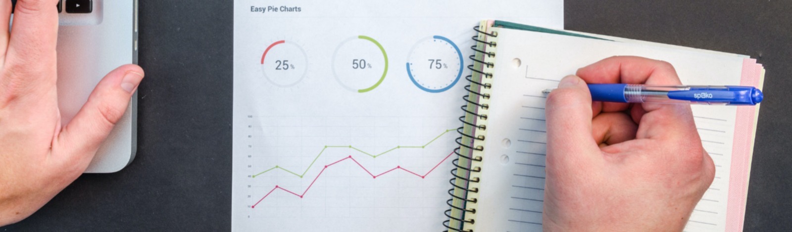 hand typing on laptop on table with paper charts